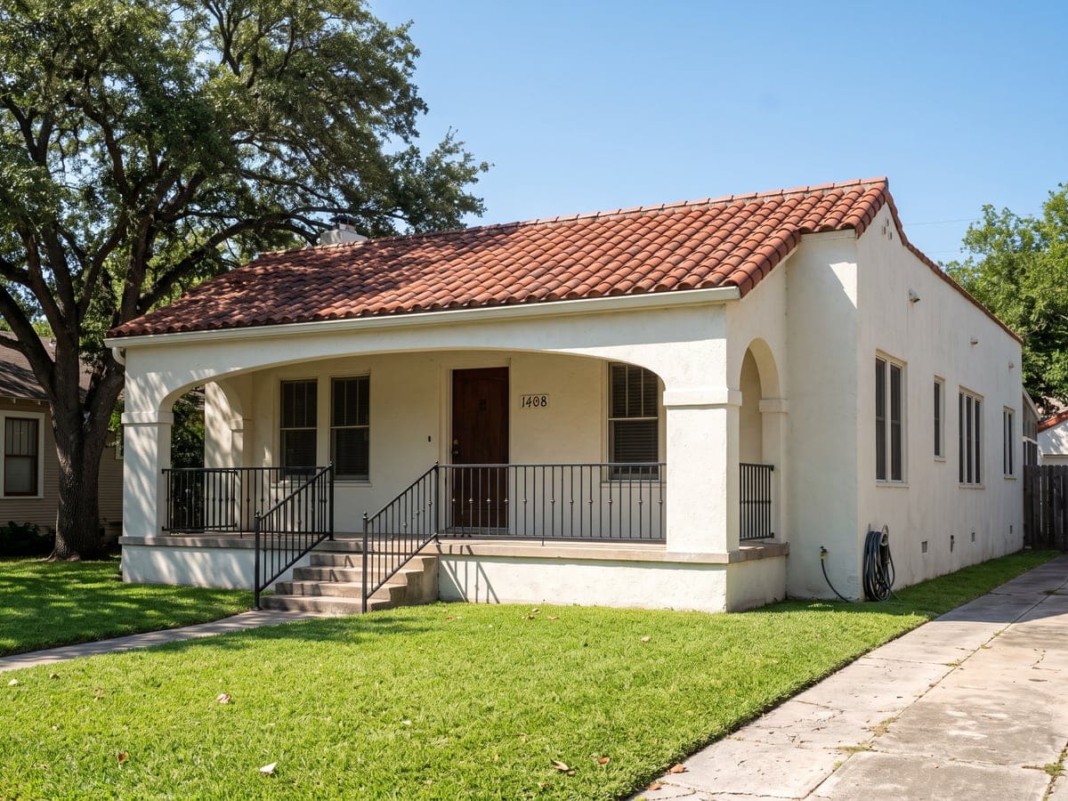 Roofing in San Antonio: a one-story Spanish revival stucco house with a red clay barrel tile roof, an arched front porch and a live oak over a trimmed lawn.