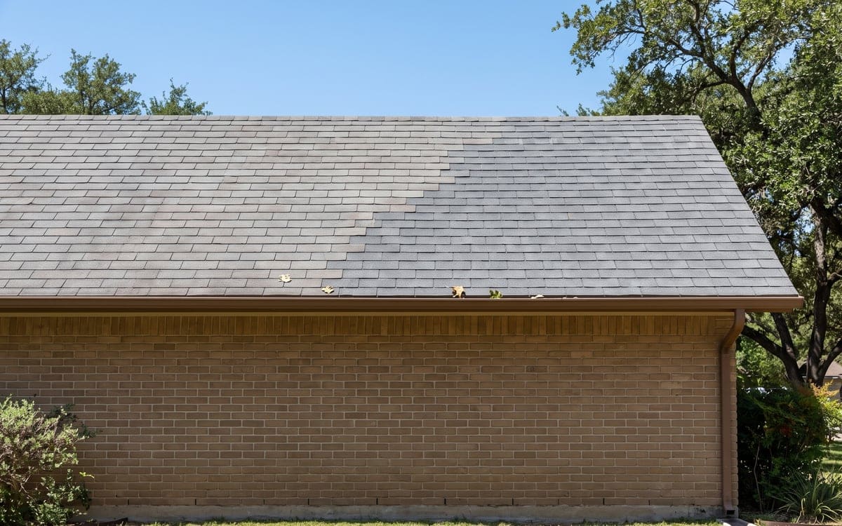 A repaired area of a gray shingle roof on a ranch house, the new shingles a shade fresher than the old, courses lined up.