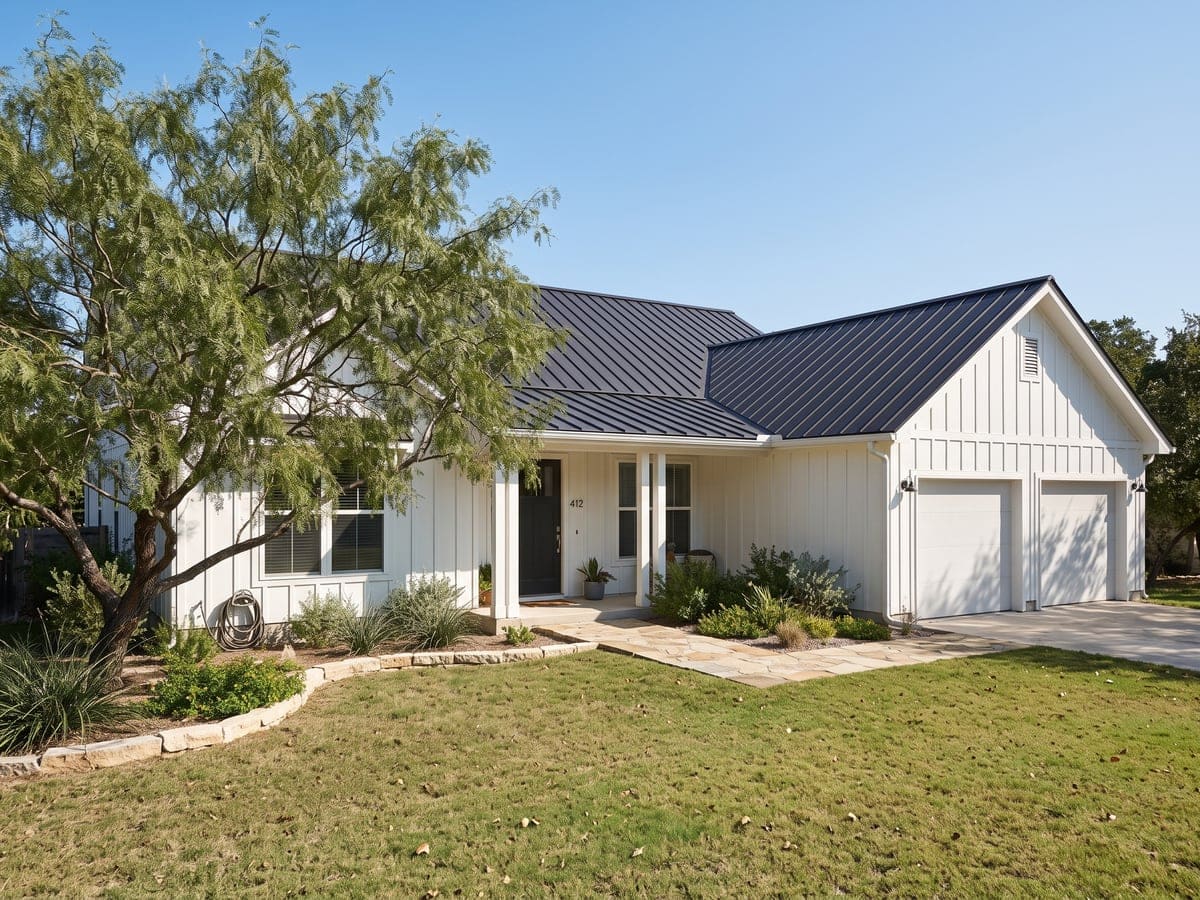 Metal roofing in San Antonio: a modern farmhouse with a black standing seam metal roof, white board-and-batten walls, a stone walk and a mesquite tree.
