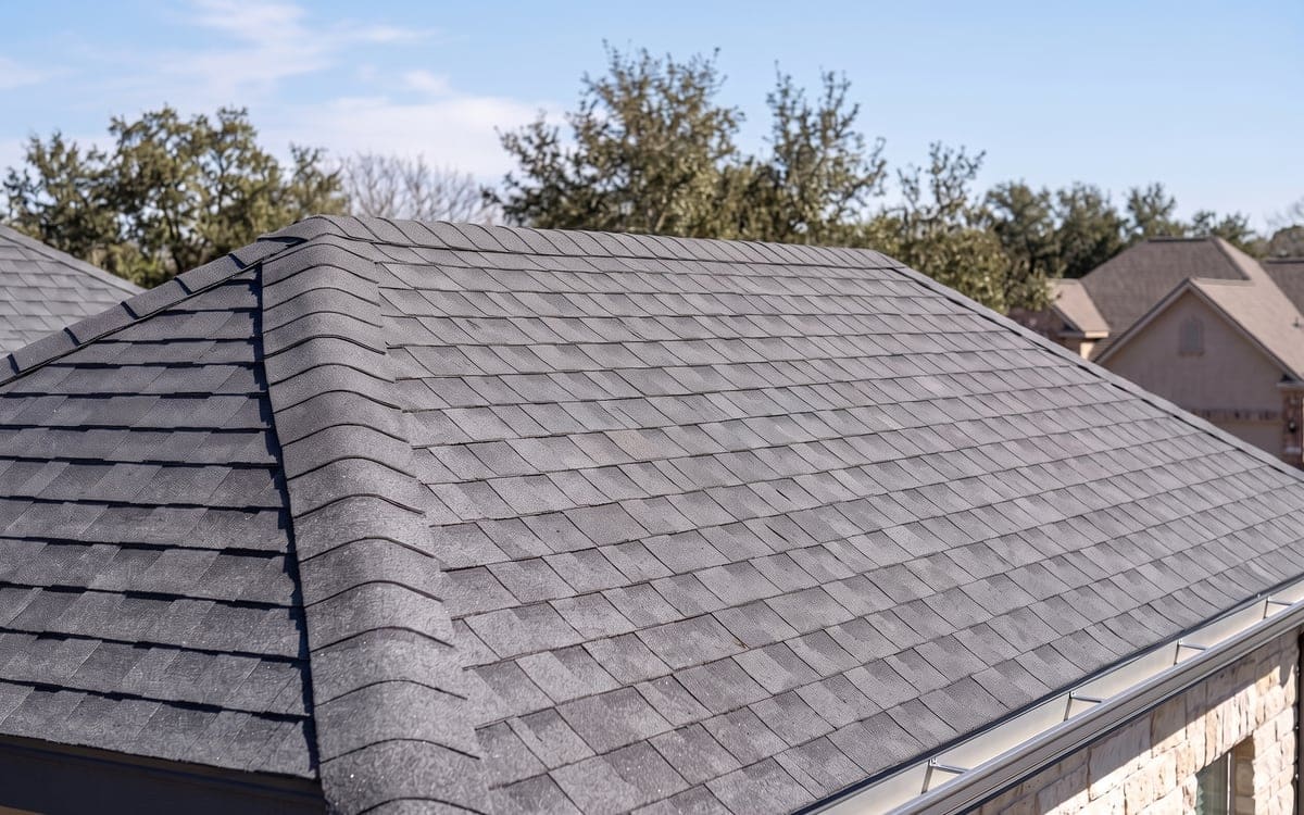A finished ridge on a new gray shingle roof, neatly lapped cap shingles.