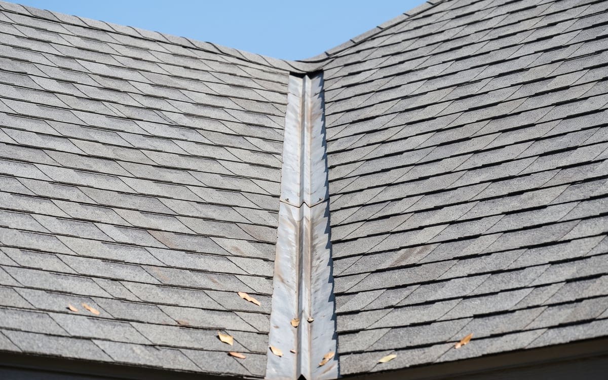 Close view of an open metal valley between two slopes of a gray shingle roof, shingles trimmed evenly along it.