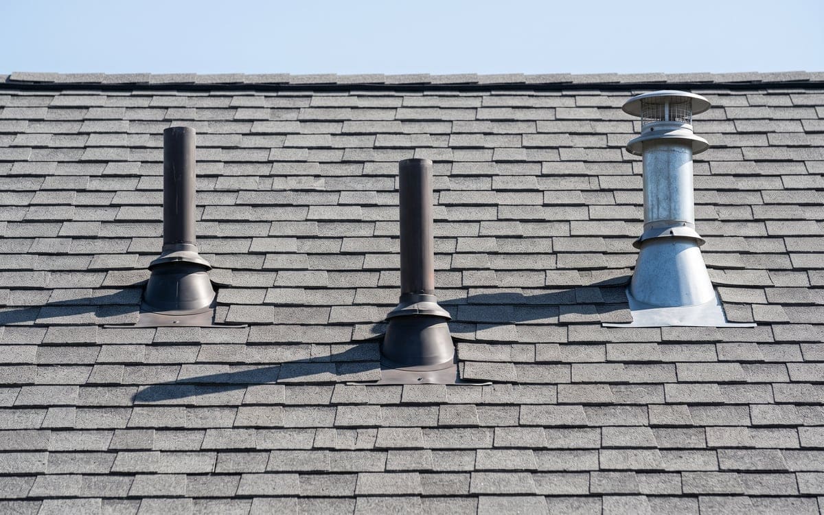 Two plumbing vent pipes and a gas flue rising through a new gray shingle roof, each with its own flashing.