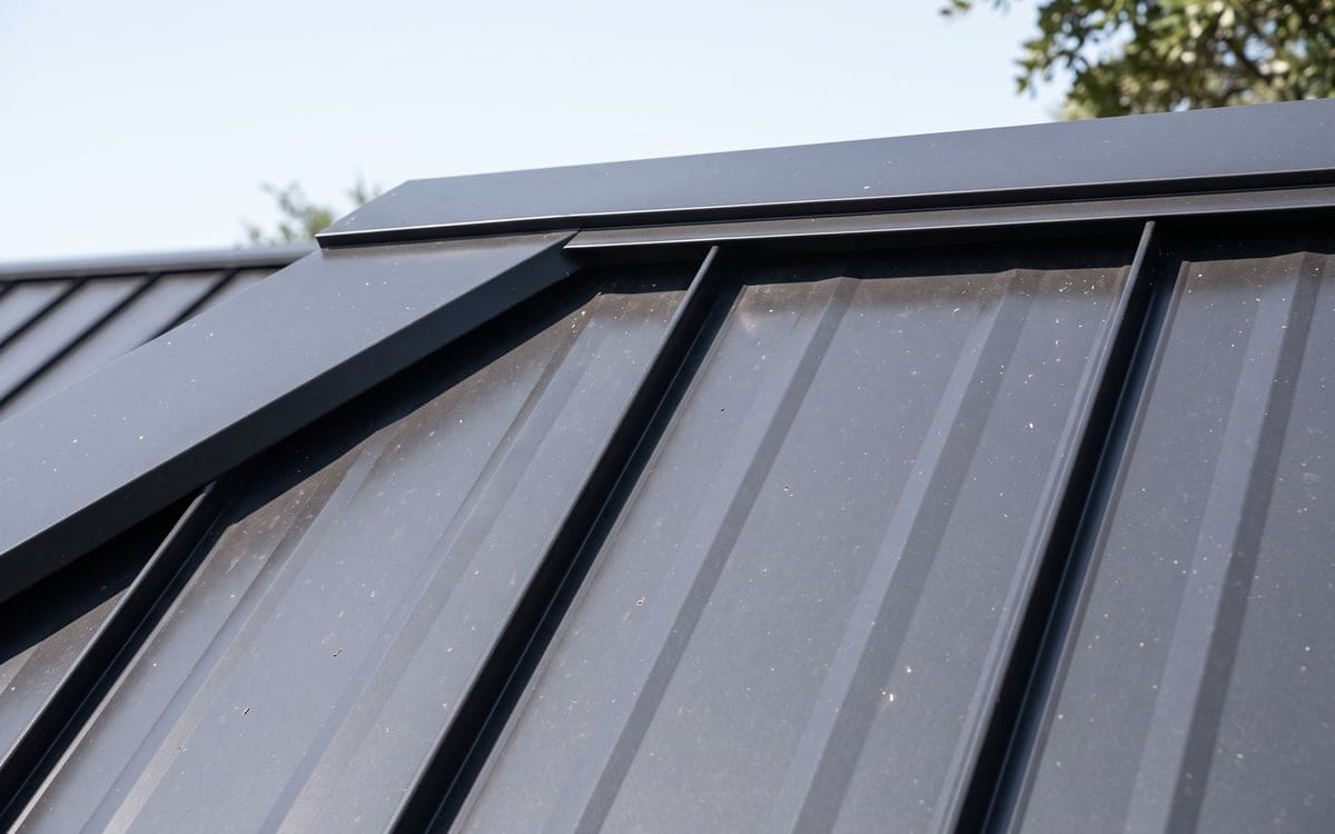 Close view of standing seam panels meeting the ridge trim on a charcoal metal roof, seams straight and evenly spaced.