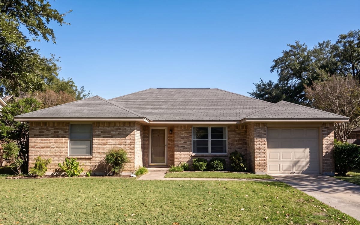 A one-story brick ranch with a simple hip roof of gray shingles and one ridge.