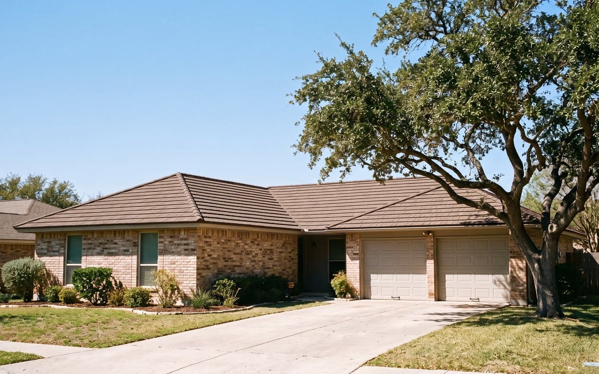 A brick ranch house with a stone-coated steel roof in a brown shake profile, a live oak beside the driveway.